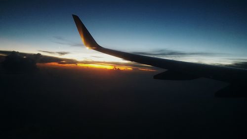 Cropped image of airplane flying against sky at sunset