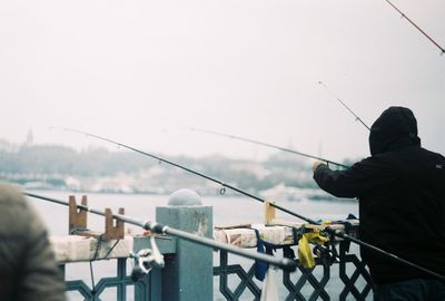 Rear view of man fishing in sea against sky