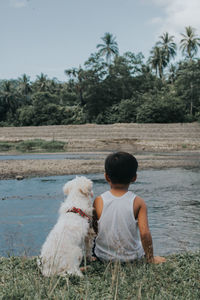 Rear view of boy with dog sitting on land