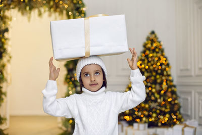 Portrait of a boy a child in a white sweater holding a gift box at the christmas tree