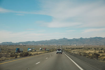 Vehicles moving on country road passing through arid landscape against sky