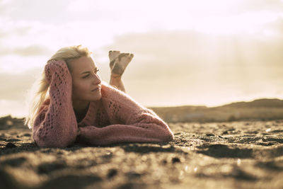 Woman lying at beach against sky during sunset