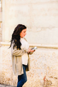 Smiling woman holding mobile phone while walking on footpath in city