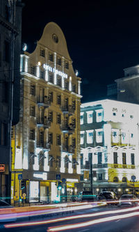 Cars on street by illuminated buildings in city at night