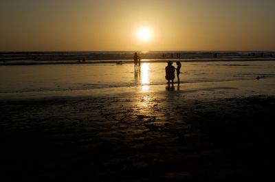 Silhouette people on beach against sky during sunset