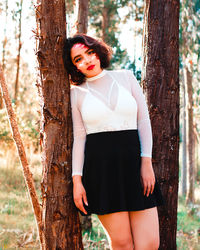 Portrait of beautiful woman standing by tree trunk