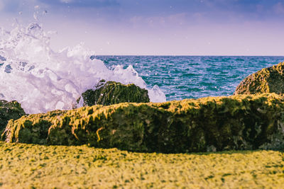 Scenic view of waves splashing on rocks at beach against sky