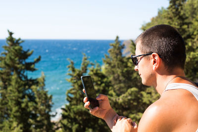 Midsection of man using mobile phone against sea