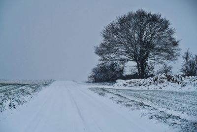 Road amidst snow covered field against sky