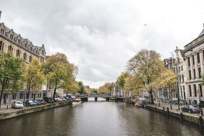 Canal amidst trees and buildings against sky