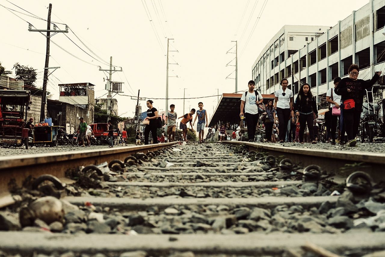 PEOPLE ON RAILROAD TRACKS IN CITY AGAINST SKY