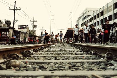 People on railroad tracks in city against clear sky