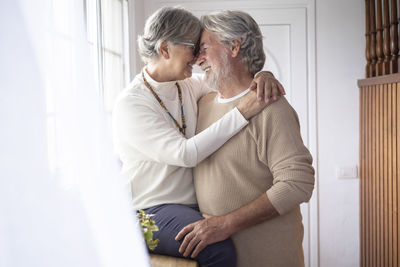 Senior couple embracing by window at home