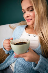 An attractive blonde is sitting on the sofa with a mug of coffee.