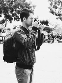 Side view of man photographing with digital camera on street