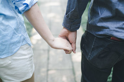 Midsection of couple holding hands while standing outdoors