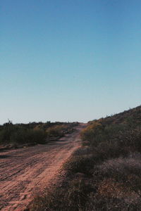 Road amidst field against clear blue sky