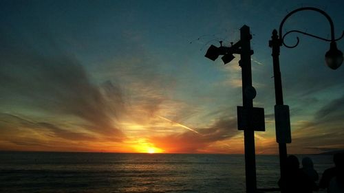 Silhouette of road sign by sea against sky during sunset