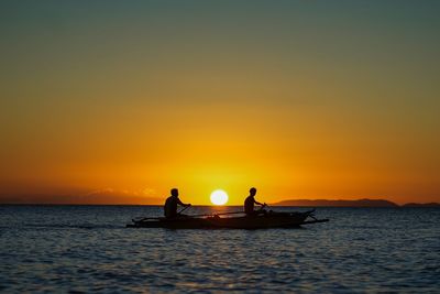 Fishermen on boat in sea against orange sky