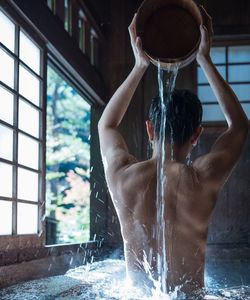 Rear view of shirtless man taking bath at home