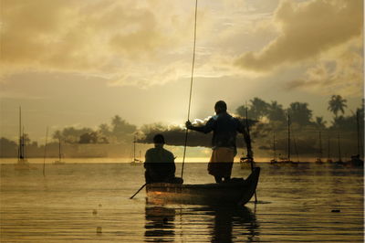 Double exposure image of fishermen sailing on boat in river against sky during sunset