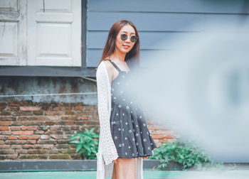 Portrait of young woman standing against brick wall