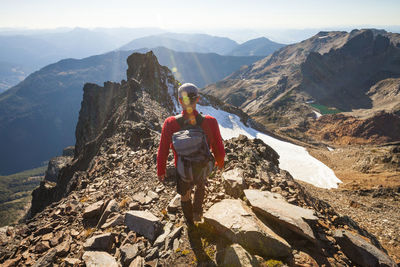 Rear view of male hiker with backpack walking on rocky mountains during sunny day