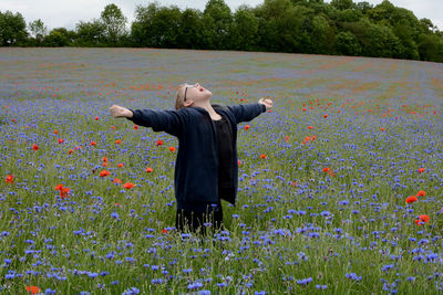 Full length of woman standing by flowers on field