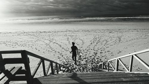 High angle view of man running with surfboard by steps at beach