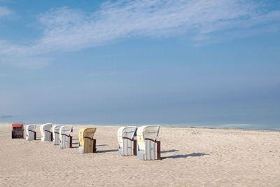 Hooded chairs on beach against sky