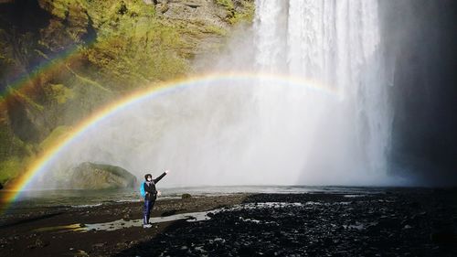 Mid adult woman standing by waterfall against rainbow