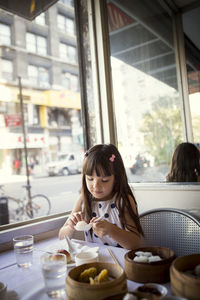 Girl looking at dumpling in spoon while sitting in restaurant