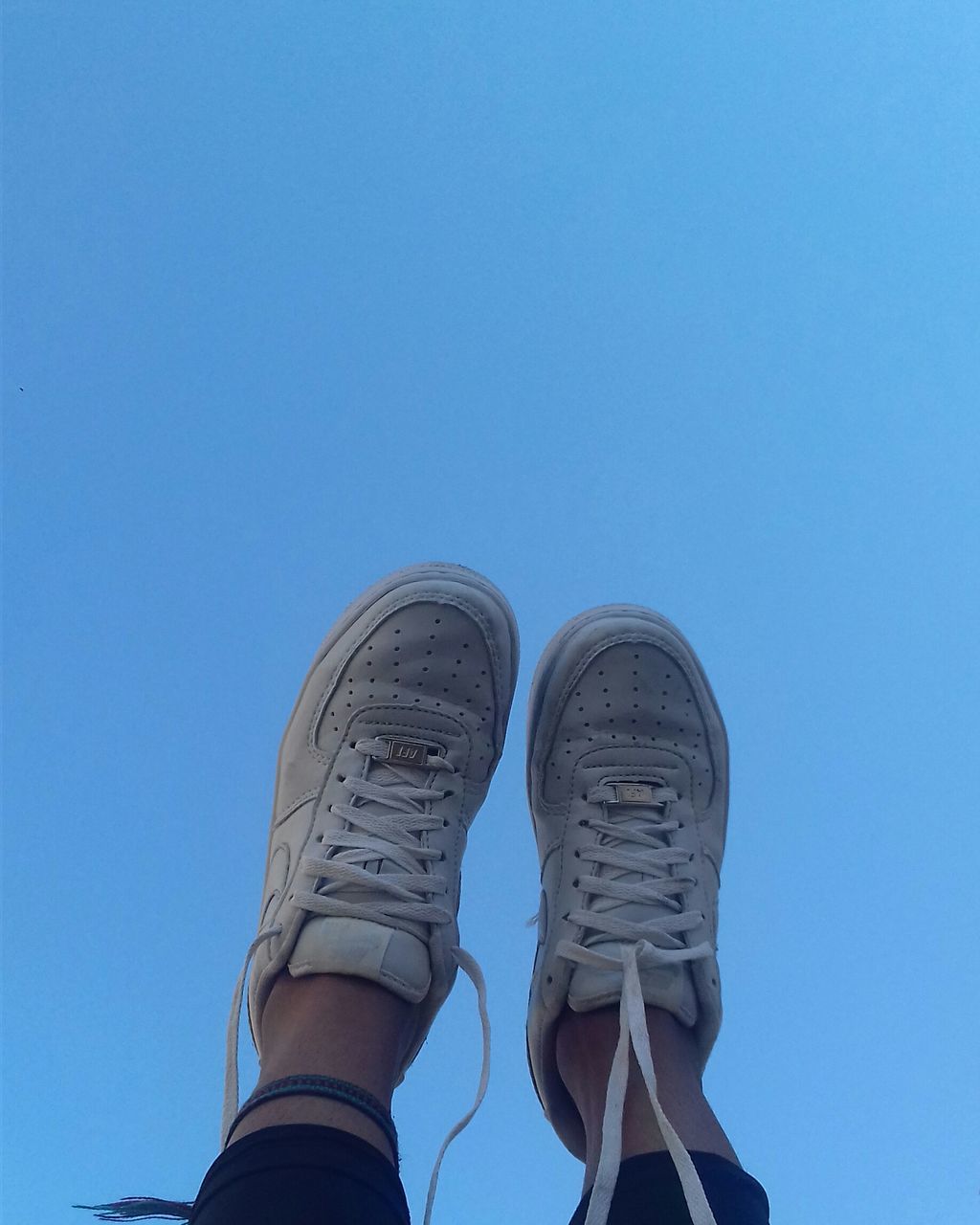 LOW SECTION OF MAN STANDING ON BLUE AGAINST CLEAR SKY