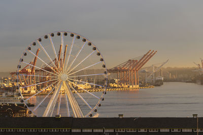 Seattle waterfront with ferris wheel and port shipping cranes at dusk.