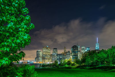 Grassy field against illuminated buildings and sky in park at night