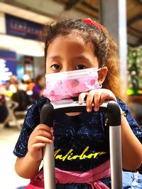 Portrait of cute girl wearing mask while holding suitcase