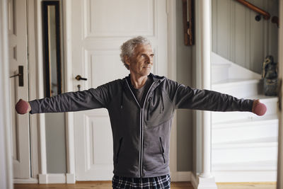 Senior man with arms outstretched exercising with dumbbells at home