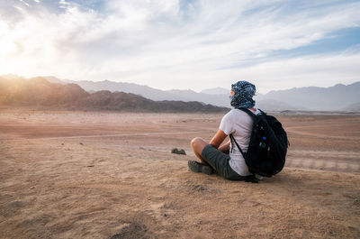 Rear view of man sitting on land against sky