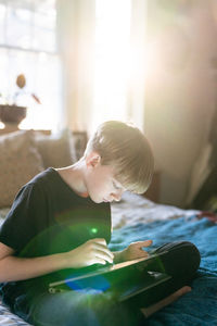 Teenager sitting on bed using stylus and 2in1 laptop computer at dusk