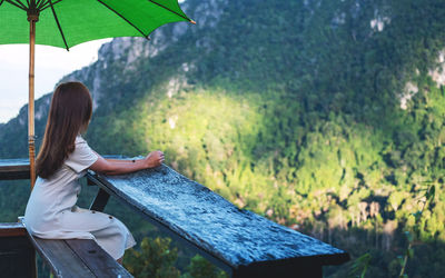 A female traveler sitting on wooden balcony and looking at a beautiful mountain and nature view