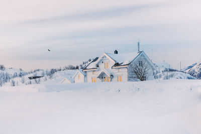 House on snow covered field by building against sky