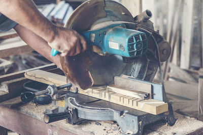 Cropped hands of worker cutting wood on electric saw in workshop