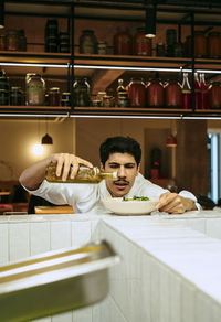 Focused male chef pouring dressing oil in salad bowl at commercial kitchen