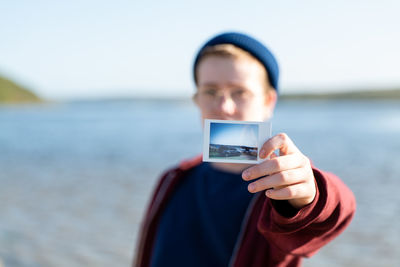 Teenager showing instant film photo to viewer with lake in background