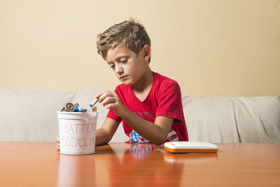Portrait of boy holding drink sitting on table at home