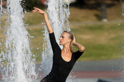 Beautiful woman with hand raised standing against fountain