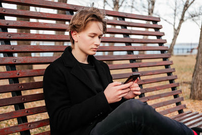 Young man using mobile phone while sitting on bench at park