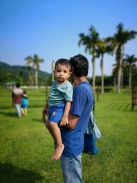 Boy standing on grass against blue sky