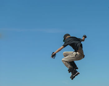 Low angle view of teenager jumping with roller skates against clear sky