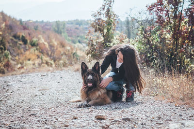 Young woman playing with dog on land against trees